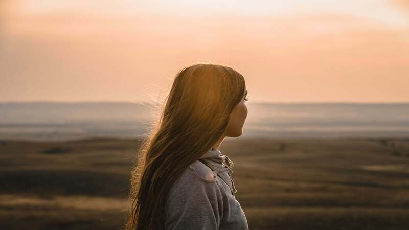 夕日を見つめながら考え事をする女性