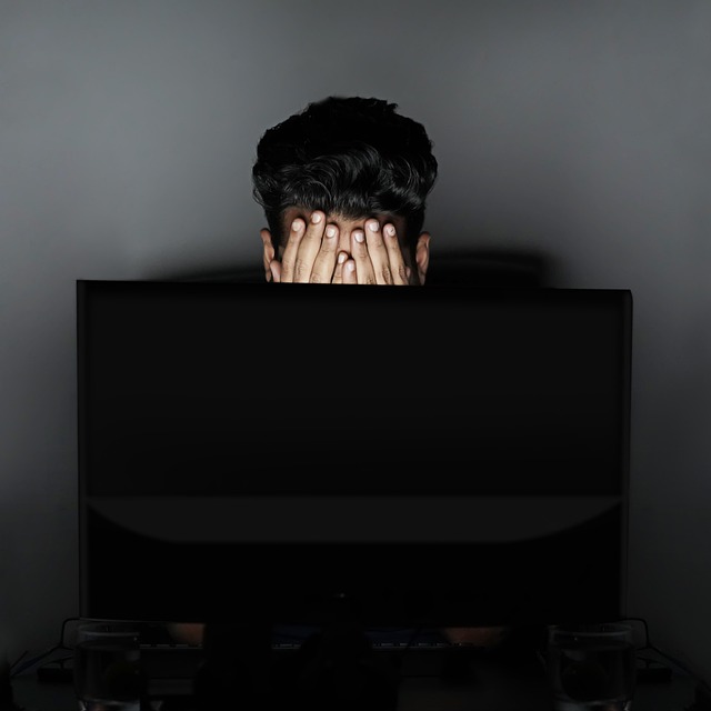 暗闇のパソコンの前で顔を覆っている人の画像